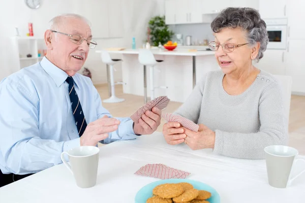 Пожилая пара весело играет в карты дома — стоковое фото