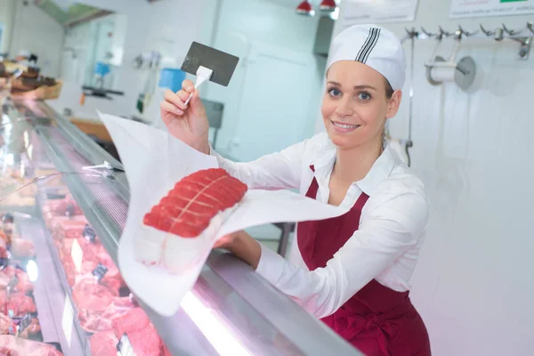 Carnicera femenina que presenta carne sobre el mostrador — Foto de Stock