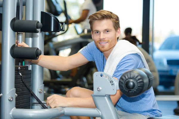 Sourire jeune homme en utilisant la machine à mouche dans la salle de gym — Photo