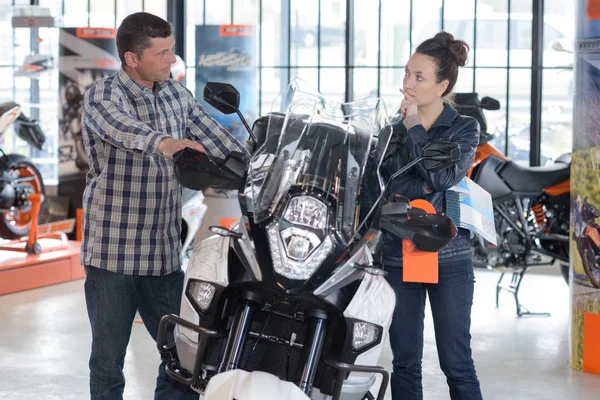 Cheerful couple looking at a motorcycle at a salon — Stock Photo, Image