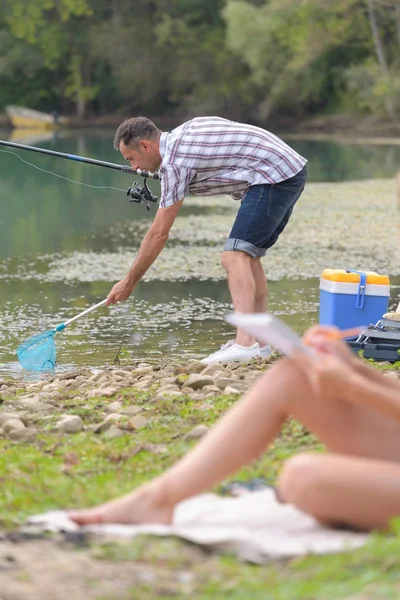Man is fishing while wife is relaxing — Stock Photo, Image