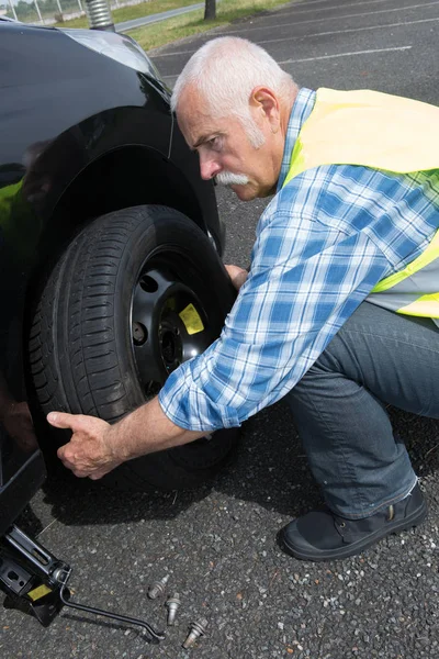 Vieil homme changeant de pneu qui fuit sur le bord — Photo