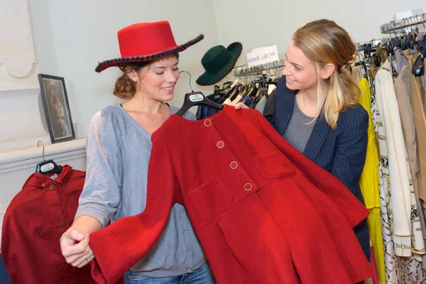 Lachende vrouw proberen op rode jas in kledingwinkel — Stockfoto