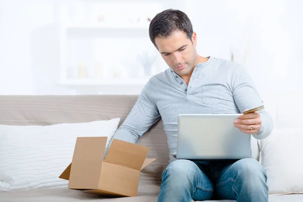Handsome man with laptop and parcel at home — Stock Photo, Image