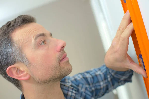 Man met behulp van waterpas op de witte muur thuis — Stockfoto