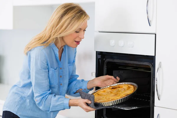 Mature blond woman baking tart in oven — Stock Photo, Image