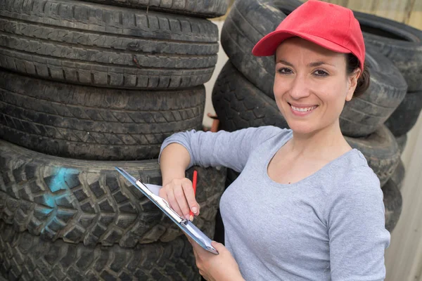 Ženské technická uprostřed hromádky pneumatik osobních automobilů — Stock fotografie