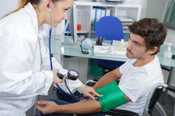 Enfermera tomando presión arterial del paciente en silla de ruedas —  Fotos de Stock