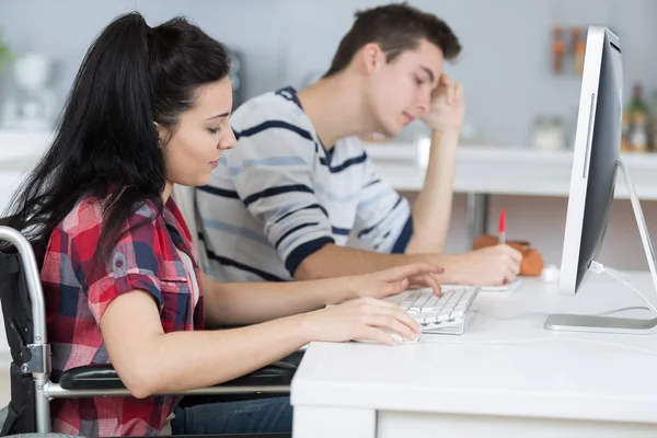 Studente in sedia a rotelle che lavora con un compagno di classe in biblioteca — Foto Stock