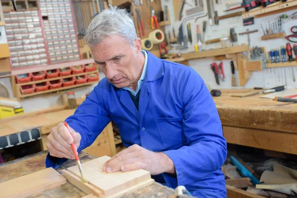 Senior Schreiner mit Pinsel auf Holzstück in Werkstatt — Stockfoto