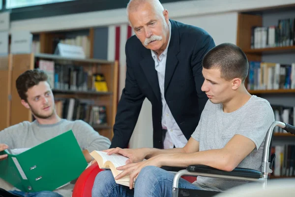 Estudiante discapacitado en la biblioteca de la escuela con su amigo y bibliotecario — Foto de Stock