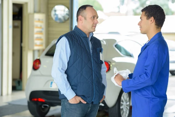 Maintenance engineer talking to male customer in car repair shop — Stock Photo, Image