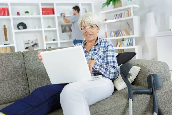 Old woman using the laptop while sitting on the sofa — Stock Photo, Image