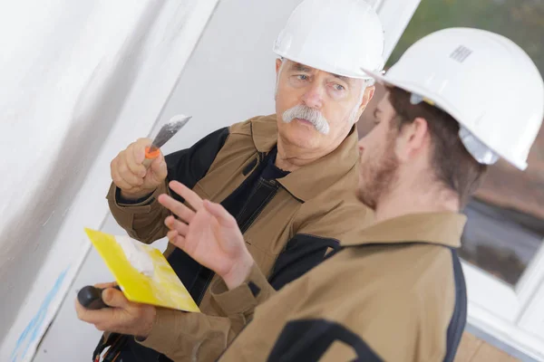 Senior builder säger apprentince hur man gips vägg med murslev — Stockfoto