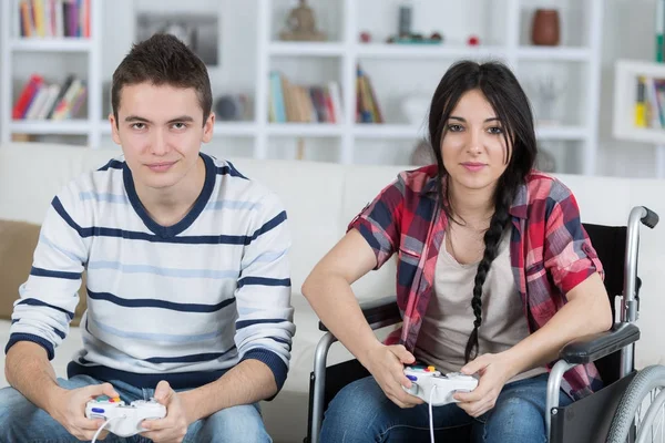 Jovem casal jogar jogos de vídeo em casa menina em cadeira de rodas — Fotografia de Stock
