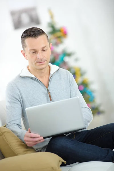 Людина використовує ноутбук, різдвяну ялинку на задньому плані — стокове фото