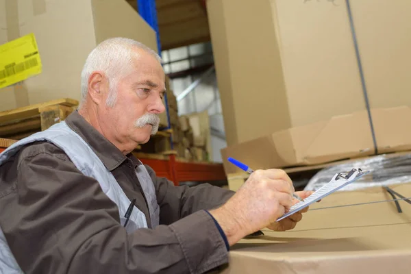 Trabajador senior escribiendo algo en su portapapeles — Foto de Stock