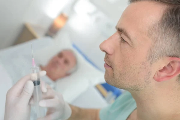 Sanitäter bereitet Spritze für Patient im Krankenhausbett vor — Stockfoto