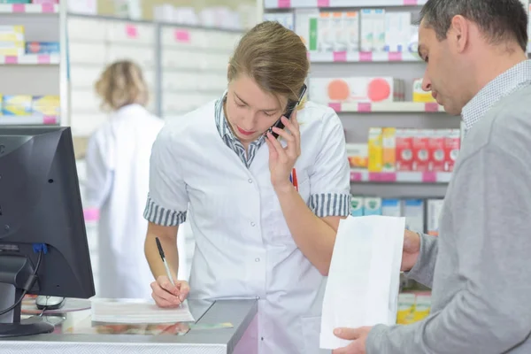 Amable mujer farmacéutica consulta paciente por teléfono en farmacia — Foto de Stock