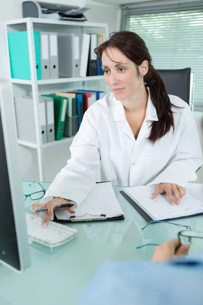 Женщина-врач выписывает медицинский рецепт, сидя в своем кабинете — стоковое фото