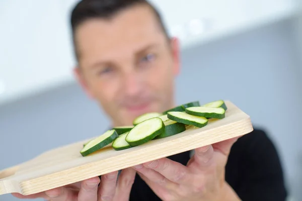 Uomo che tiene cetriolo affettato sul tagliere — Foto Stock