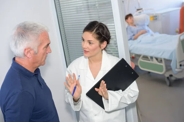 Krankenschwester spricht mit Familienangehörigen außerhalb des Patientenzimmers — Stockfoto