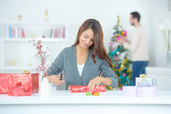 Schöne junge Frau, die ein Geschenk im Wohnzimmer einwickelt — Stockfoto