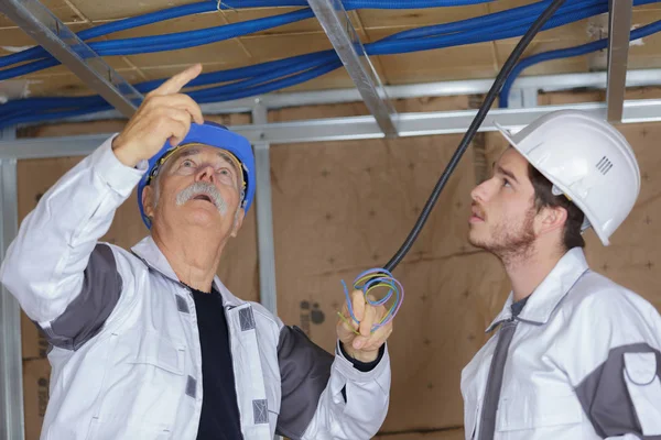 Loodgieter en leerling houden een blauwe pijp boven een plafond — Stockfoto