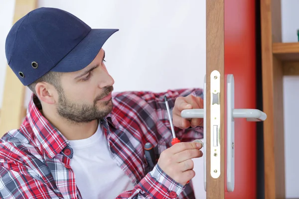 Jovem consertando a porta com chave de fenda — Fotografia de Stock