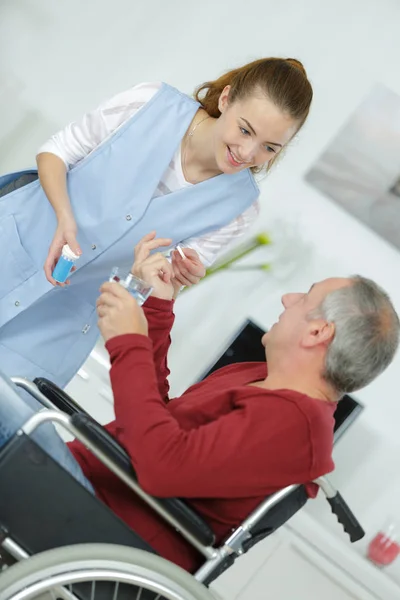 Mujer joven dando hombre en silla de ruedas píldora médica —  Fotos de Stock