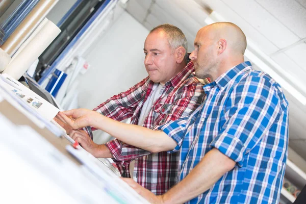 Два человека загружают новый рулон в промышленный принтер — стоковое фото