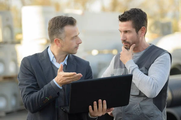 Gerente y trabajador hablando fuera y utilizando un ordenador portátil — Foto de Stock