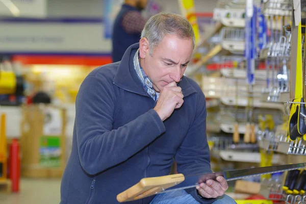 Uomo sceglie di una sega a mano in negozio — Foto Stock