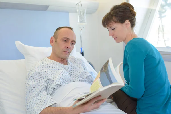 Людина в лікарні з відвідувачем читає брошуру — стокове фото
