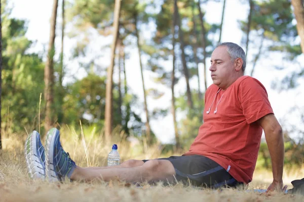Middle aged man sat on ground while out exercising — Stock Photo, Image