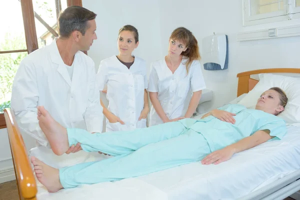 Enfermeiras estudantis assistindo médico levantar a perna do paciente — Fotografia de Stock