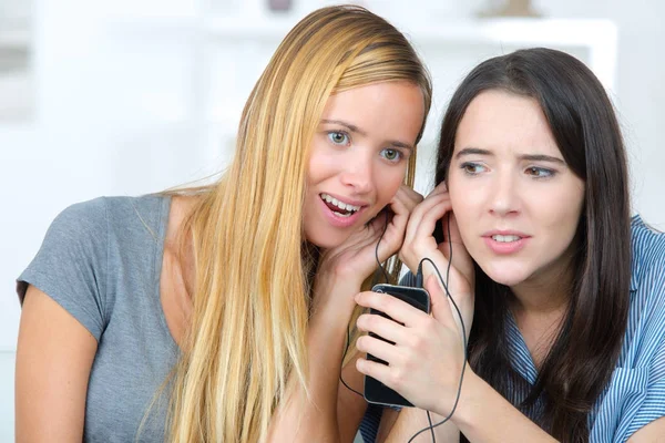 Dois companheiros de quarto ouvindo a mesma conversa móvel em casa — Fotografia de Stock