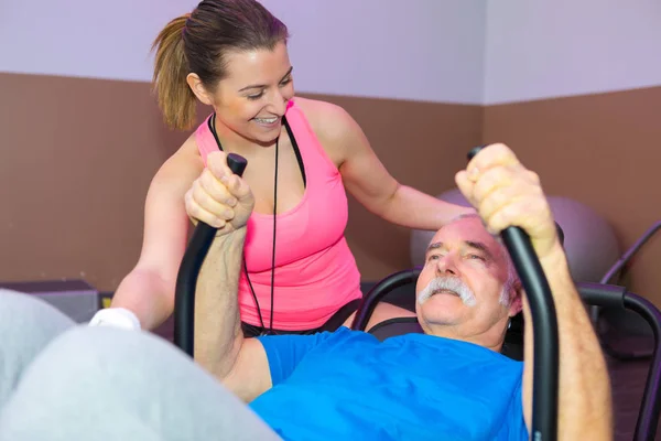 Terapeuten uppmuntrar äldre man i fitnesstudio — Stockfoto