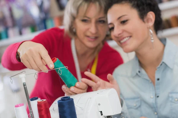 Dos mujeres sonrientes usando máquina de coser mientras sostienen tela brillante —  Fotos de Stock