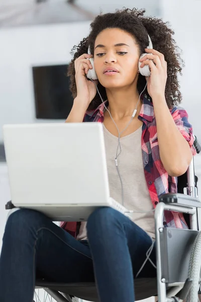 Junge Frau im Rollstuhl mit Laptop und Kopfhörer — Stockfoto