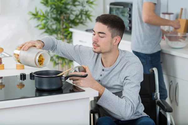 Joven discapacitado en silla de ruedas cocinando una comida en la cocina — Foto de Stock