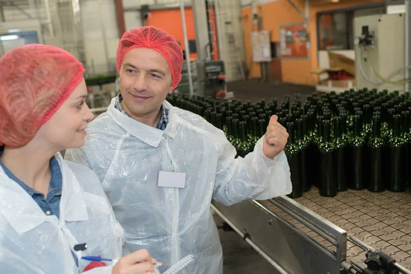 Technicus coleagues controle verpakkingslijn op het bottelen van vervaardiging — Stockfoto