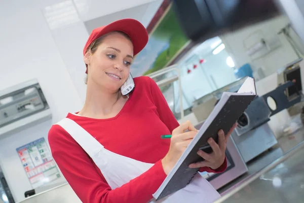 Female butcher on the phone behind counter — Stock Photo, Image