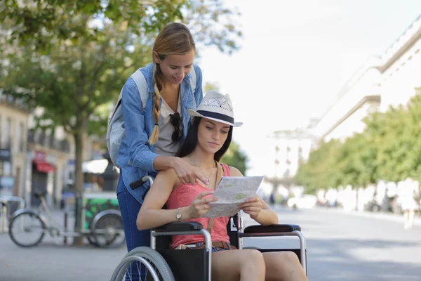 Deux amis visitant la ville étrangère un assis en fauteuil roulant — Photo