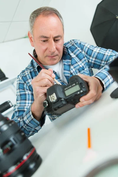 Fokussierter Mann mittleren Alters repariert Retro-Kamera an seinem Arbeitsplatz — Stockfoto