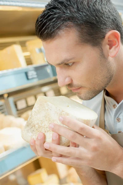 Cheese shop worker smelling on of his cheeses — Stock Photo, Image