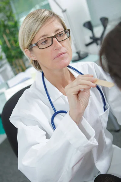 Arzt hält hölzernes Gerät in der Hand, um den Hals des Patienten zu kontrollieren — Stockfoto