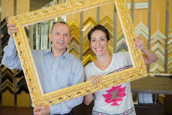 Middle aged man and woman looking through empty picture frame — Stock Photo, Image