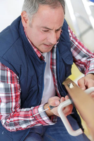 Man van middelbare leeftijd tot vaststelling van de deur met schroevendraaier — Stockfoto