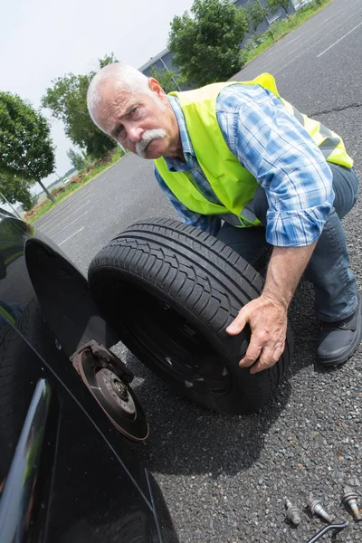 Vieil homme changeant de pneu qui fuit sur le bord — Photo